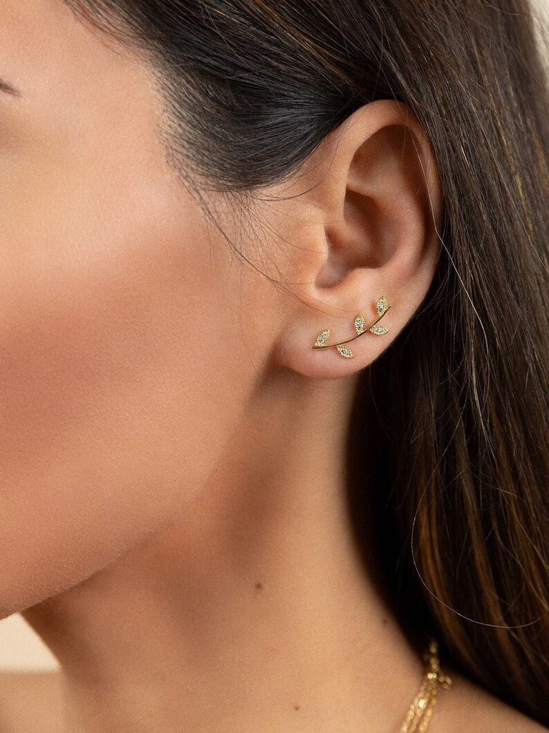 May include: Gold leaf earrings with small clear cubic zirconia stones. The earrings are shaped like a branch with leaves.