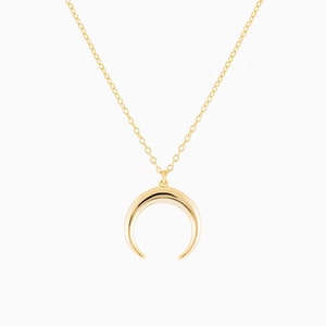 Puede incluir: Un collar de oro con un colgante de media luna.