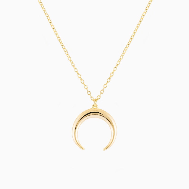 Puede incluir: Un collar de oro con un colgante de media luna.