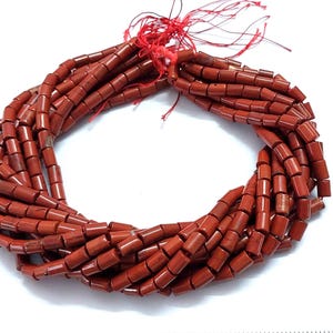 May include: A strand of red gemstone beads, each bead is a cylinder shape. The beads are strung on a red thread.