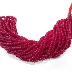 May include: A strand of deep red glass beads, approximately 4mm in diameter. The beads are round and have a smooth, glossy finish.