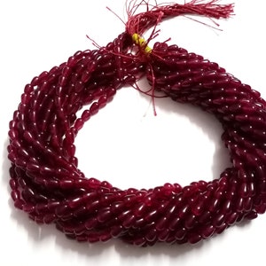 May include: A bundle of deep red, oval-shaped beads, tightly strung together. The beads have a glossy finish and are arranged in a spiral pattern. A red tassel is attached at the top. The background is plain white.