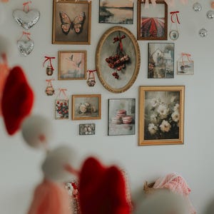 May include: A white wall decorated with a garland of pink and red hearts, framed pictures, and a variety of other decorative items. The pictures include a butterfly, a bouquet of flowers, a landscape, and a still life.