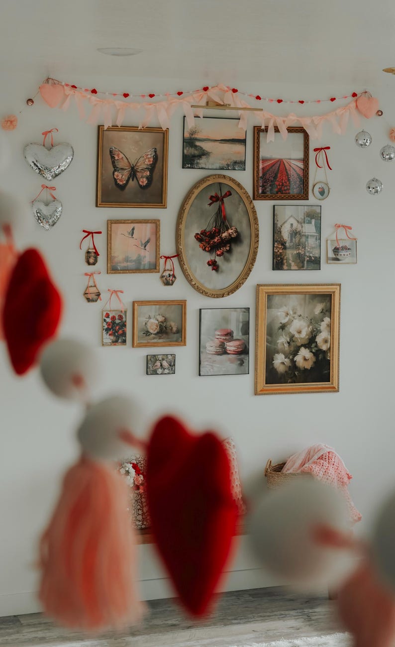 May include: A white wall decorated with a garland of pink and red hearts, framed pictures, and a variety of other decorative items. The pictures include a butterfly, a bouquet of flowers, a landscape, and a still life.