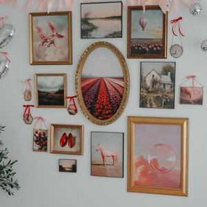 May include: A gallery wall with a variety of framed artwork, including landscapes, florals, and abstract designs. The wall is decorated with a pink and red heart garland.