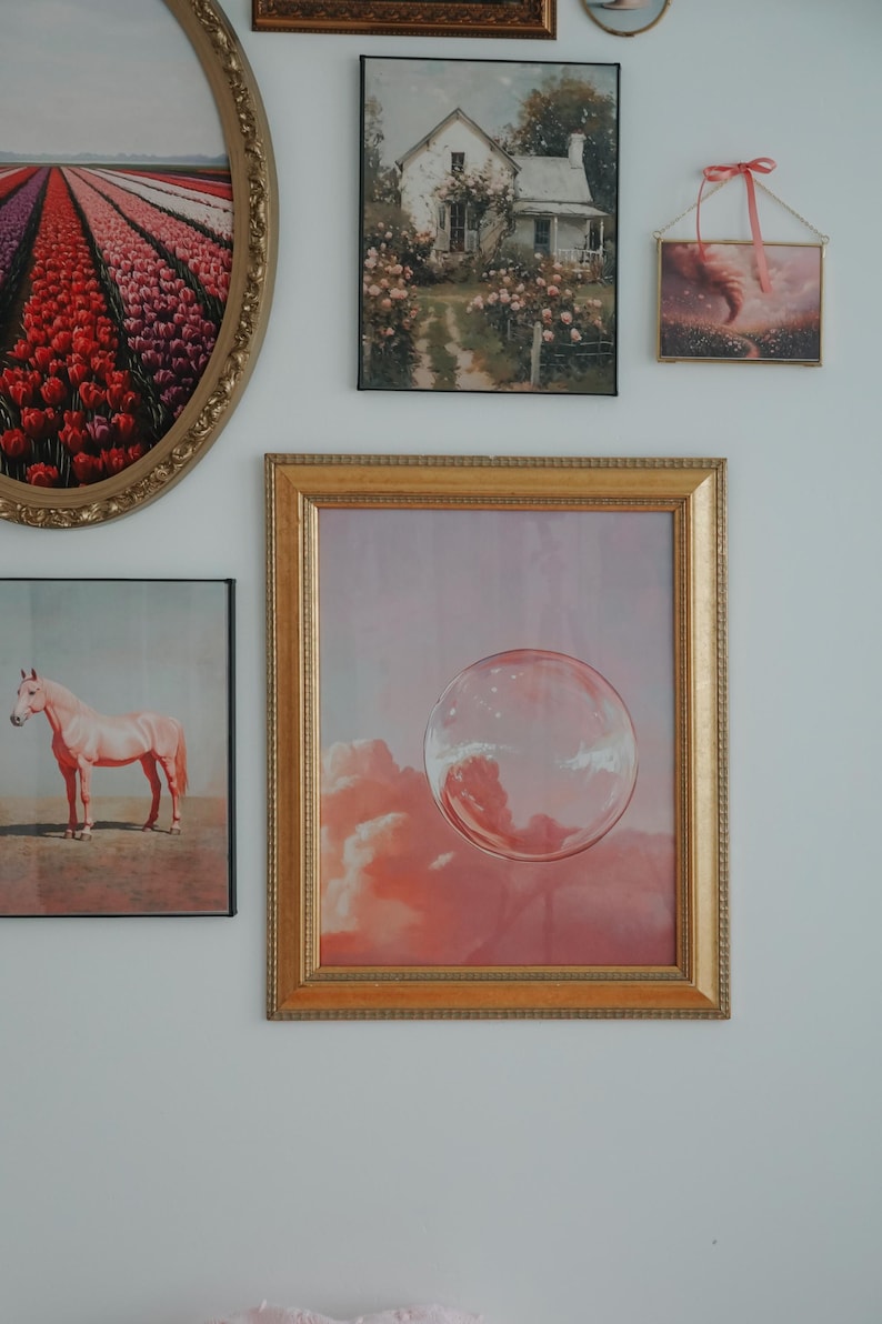 May include: A gallery wall with various framed artwork, including a pink horse, a house in a garden, a field of tulips, and a bubble floating in a pink sky.