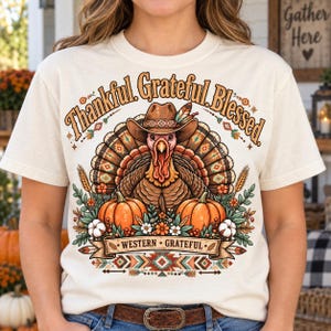 Może przedstawiać: Kremowy t-shirt z grafiką indyka w kowbojskim kapeluszu, otoczonego dyniami, pszenicą i kwiatami. Tekst głosi Thankful Grateful Blessed oraz Western Grateful. Projekt zawiera geometryczne wzory i jesienne kolory w odcieniach brązu i pomarańczu.