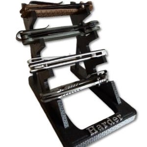May include: A black knife display stand holding several folding knives. The stand has three tiers and the word "Harder" is displayed on the base. The knives have various handle designs and blade styles.