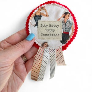 Könnte beinhalten: Ein handgefertigtes Stoffabzeichen mit rotem, gewelltem Rand und einem weißen Mittelteil mit Illustrationen von Frauen im Vintage-Stil. Das Abzeichen enthält den Text "Itty Bitty Titty Committee" auf einem rechteckigen Aufnäher, mit rot-weiß gepunkteten Bändern.