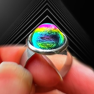 May include: A silver-toned ring featuring a large, smooth, dome-shaped cabochon stone. The stone displays a vibrant, iridescent spectrum of colors, including bright green, blue, purple, and yellow, with a swirling, reflective surface texture.