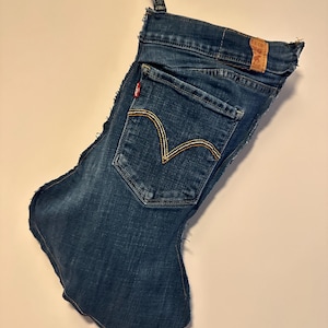 May include: A Christmas stocking made from repurposed blue denim jeans. The stocking features the back pocket of the jeans with the signature stitching and a red Levi's tag. A loop is attached for hanging.