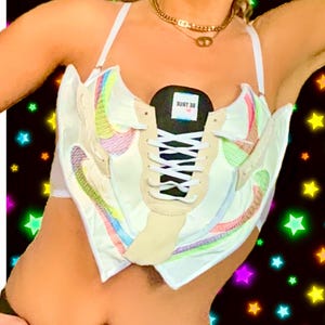 May include: A white crop top with a rainbow design, featuring a pair of white sneakers with black laces and a black tongue that says "BE TRUE".