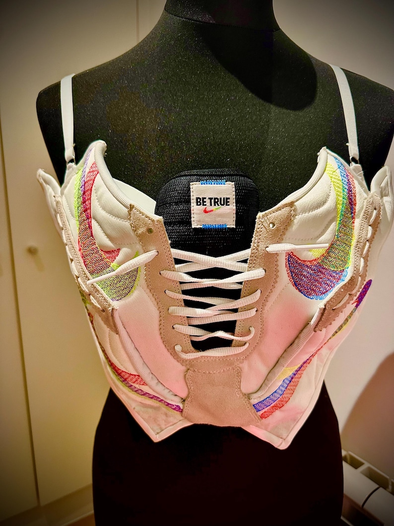 May include: A white corset made from a pair of Nike sneakers with rainbow colored accents and a black tag that says "BE TRUE".