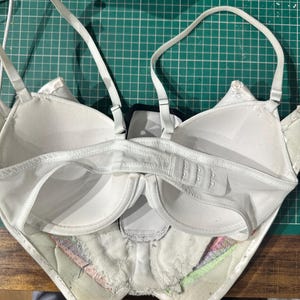 May include: White bra with adjustable straps and a hook and eye closure in the back. The bra is turned inside out, showing the lining and the seams.