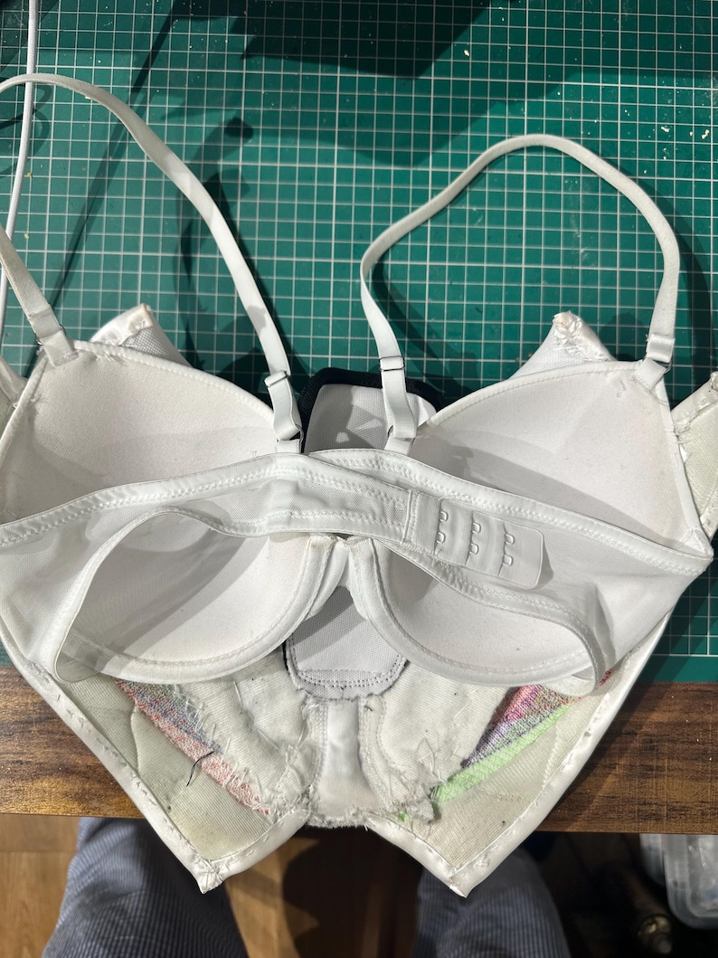 May include: White bra with adjustable straps and a hook and eye closure in the back. The bra is turned inside out, showing the lining and the seams.