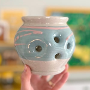 May include: A light blue and pink ceramic diffuser with holes for scent to escape. The diffuser has a white glaze and a pink and blue swirl design.