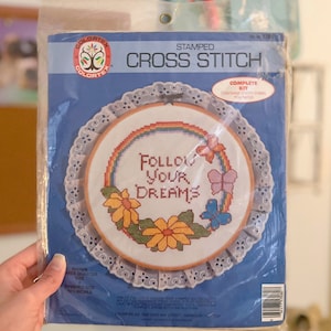 May include: A complete cross stitch kit featuring a white embroidery hoop with a colorful rainbow, flowers, and butterflies surrounding the text "Follow Your Dreams".