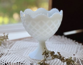 May include: White milk glass pedestal bowl with a diamond pattern. The bowl is sitting on a white crocheted doily.