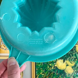 Pode incluir: Um espremedor de citrinos de pl&aacute;stico azul turquesa com uma pega. O espremedor tem um design de estrela e o texto "Dixieware Stock No. L-13 Made in U.S.A." impresso na parte inferior.