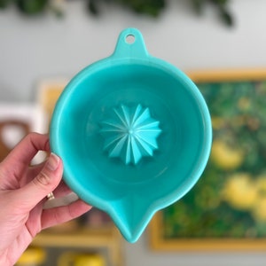 Pode incluir: Um espremedor de citrinos azul turquesa com um espremedor em forma de estrela no centro. O espremedor tem uma pega e um bico para verter.