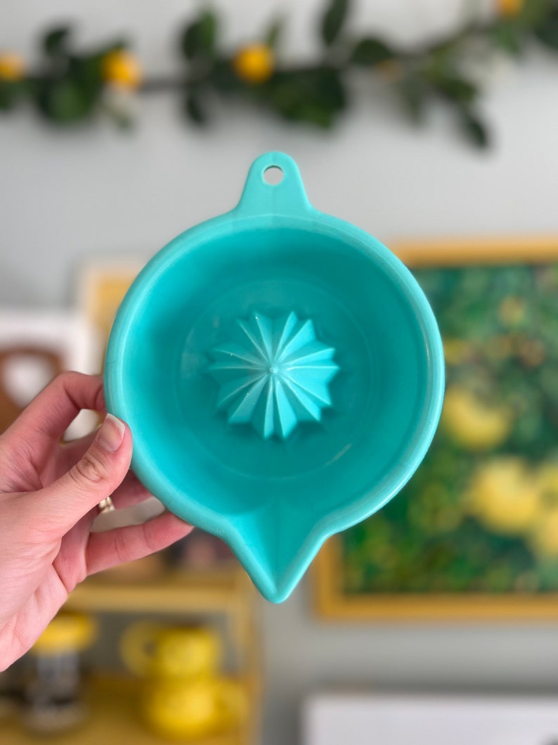 Pode incluir: Um espremedor de citrinos azul turquesa com um espremedor em forma de estrela no centro. O espremedor tem uma pega e um bico para verter.