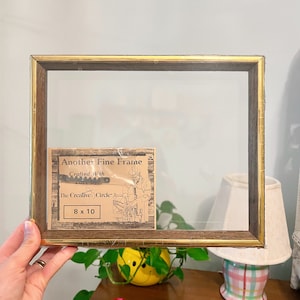 Può includere: Una cornice dorata con finitura in legno. La cornice contiene un biglietto che recita "Another Fine Frame Crafted With The Creative Circle 8 x 10".