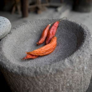 May include: Three dried red chilli peppers in a grey stone mortar and pestle.