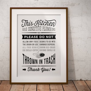 May include: Black and white sign with the text "This Kitchen Has Sensitive Plumbing. Please Do Not Allow Any Food Debris To Go Into The Drain Or Use Garbage Disposal. All Food Debris, Cooking Oils, Grease, Egg Shells, Coffee Grounds Should Be Thrown In Trash. Thank You!"