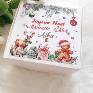 K&ouml;nnte beinhalten: Eine wei&szlig;e Geschenkbox mit weihnachtlichem Design. Die Box zeigt Illustrationen eines Rentiers, eines Lebkuchenmanns, Ornamente und ein verpacktes Geschenk. Auf der Box steht "Joyeux No&euml;l" und "Ma&icirc;tresse Chlo&eacute; Alba."