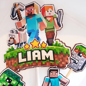 Peut inclure: Un ensemble de décorations de gâteau sur le thème de Minecraft avec Steve, Alex, un loup et un Creeper avec de la TNT. La pièce centrale affiche le nom LIAM en lettres capitales sur un bloc de terre herbeux, avec trois étoiles et un chiffre neuf.