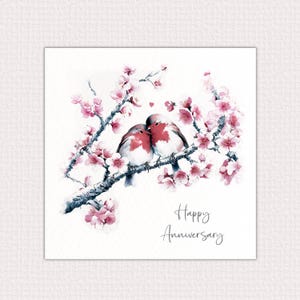 May include: A greeting card featuring a watercolour illustration of two robins perched on a branch of a flowering tree. The birds are facing each other and appear to be kissing. The text "Happy Anniversary" is printed below the image.