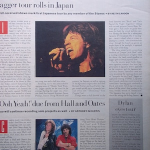 May include: A black and white photo of Mick Jagger performing on stage in Japan. He is holding a microphone and singing into it. The stage is lit with bright lights and there is a large crowd in the background.