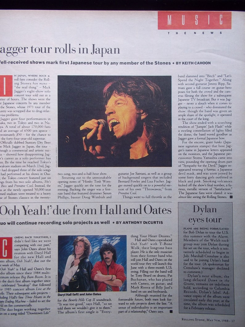 May include: A black and white photo of Mick Jagger performing on stage in Japan. He is holding a microphone and singing into it. The stage is lit with bright lights and there is a large crowd in the background.