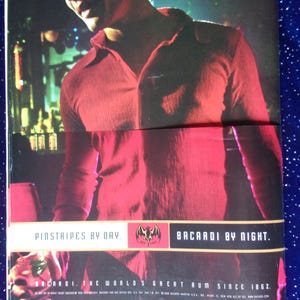 May include: A man wearing a red shirt with the text "Pinstripes by Day. Bacardi by Night. Bacardi. The World's Great Rum Since 1862." printed on the bottom.