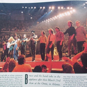 May include: A group of musicians on stage in front of a large crowd. The musicians are taking in the applause after their performance. The text on the page reads "Bruce and the band take in the applause after their March 23rd show at the Omni, in Atlanta."