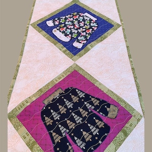 Peut inclure: Chemin de table de Noël matelassé avec trois sections en forme de losange. La section centrale présente une combinaison noire avec des sapins dorés. Les autres sections ont une combinaison rouge et bleue avec un motif festif. Fond rose floral.
