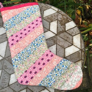 Könnte beinhalten: Ein rosa-blauer Patchwork-Weihnachtsstrumpf mit Blumenmuster. Der Strumpf besteht aus Stoffresten, die diagonal zusammengenäht wurden.