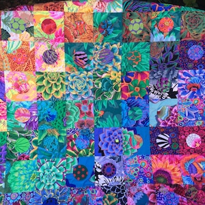 Pode incluir: Um edredom vibrante com um design de patchwork de padrões florais e botânicos coloridos. Os quadrados exibem uma variedade de flores e suculentas em tons de rosa, azul, verde e laranja. O design do edredom é uma mistura de motivos florais abstratos e realistas.