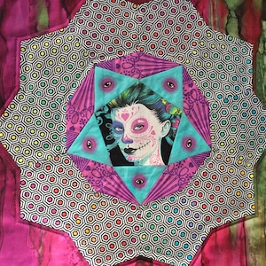 May include: A colorful quilt block with a central image of a woman with a sugar skull makeup design. The block is surrounded by a black and white geometric pattern.