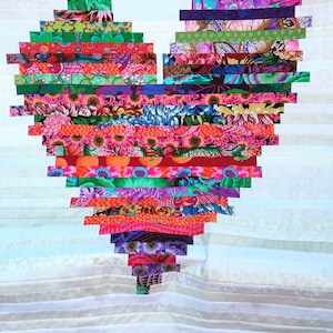 Peut inclure: Une courtepointe en forme de cœur colorée faite de bandes de tissu dans différents motifs et couleurs, notamment le rouge, l'orange, le jaune, le vert, le bleu, le violet et le blanc.