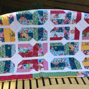 May include: A patchwork quilt with a white background and colorful squares. The squares are made of different fabrics with floral patterns in shades of pink, red, yellow, blue, and green.