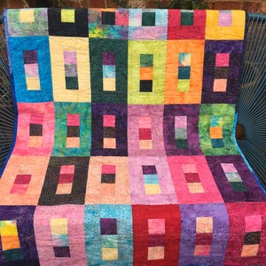 May include: A colorful patchwork quilt with a vibrant array of squares and rectangles in shades of blue, pink, orange, green, and purple. The quilt is draped over a blue chair, showcasing its intricate design and craftsmanship. The quilt's dimensions are not visible.