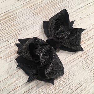 May include: A black sparkly hair bow with a large, double-looped bow and a smaller, single-looped bow.