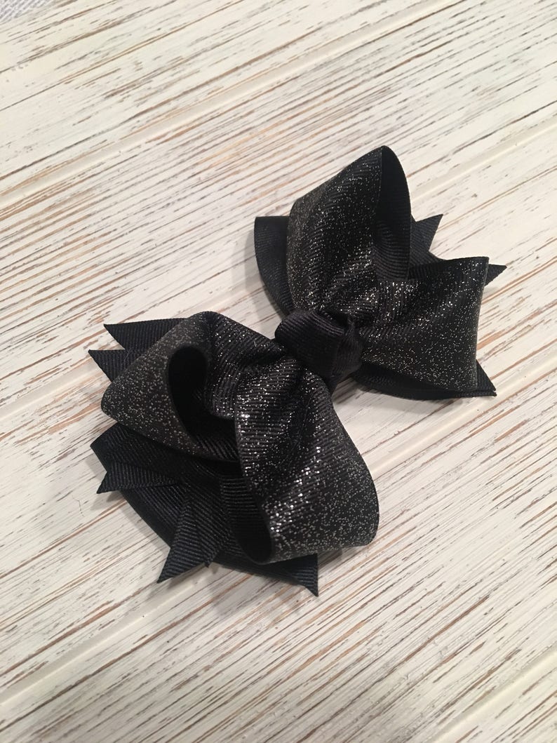 May include: A black sparkly hair bow with a large, double-looped bow and a smaller, single-looped bow.