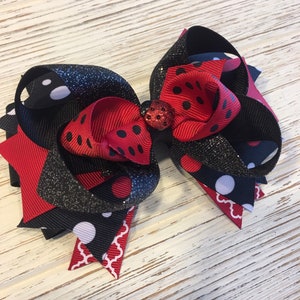 May include: A large red and black bow with white polka dots and a black glitter ribbon. The bow has a small red ladybug embellishment in the center.