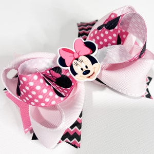 May include: Pink and white bow with a black and white chevron pattern and pink polka dots. The bow features a Minnie Mouse character with a pink bow.