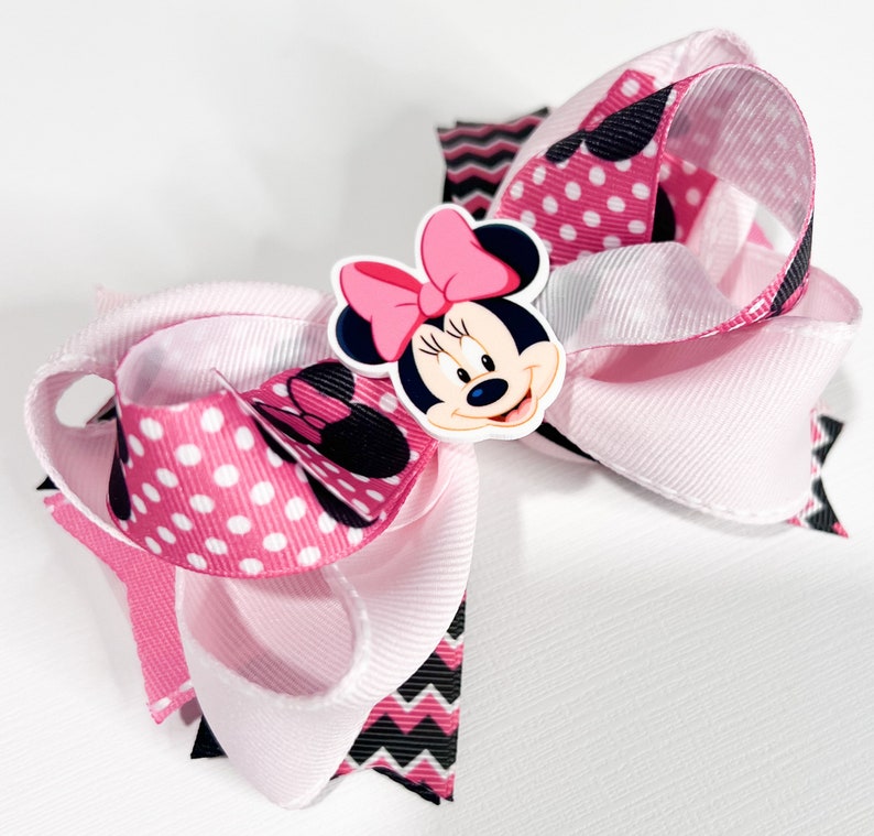 May include: Pink and white bow with a black and white chevron pattern and pink polka dots. The bow features a Minnie Mouse character with a pink bow.