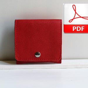 Puede incluir: Una pequeña cartera de cuero roja con cierre de botón plateado.