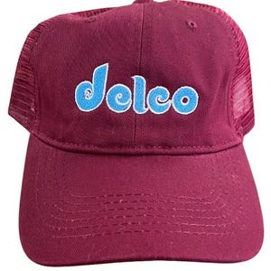 May include: A maroon trucker hat with a blue and white embroidered logo that says "Delco".