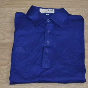 May include: A blue polo shirt with a white label that says "Pringle". The shirt has a button-up collar and a pocket on the left side.